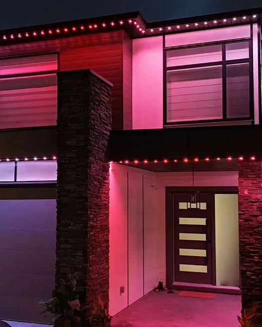 A modern flat-roof house with a red and white roofline and a lit stone column.