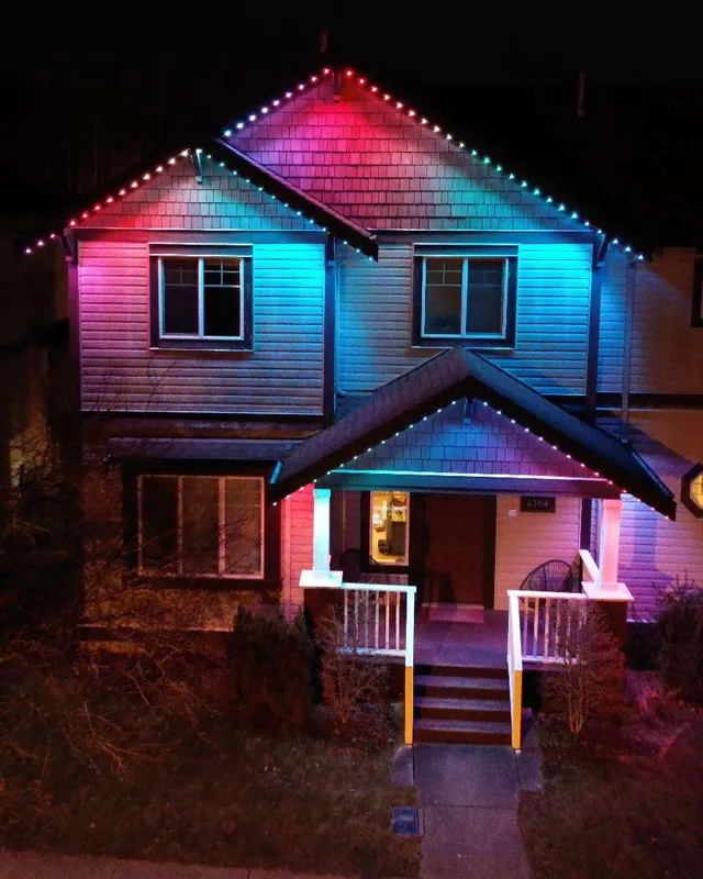 A two-storey craftsman-style house with a rainbow of colour along its gables, lit at night.