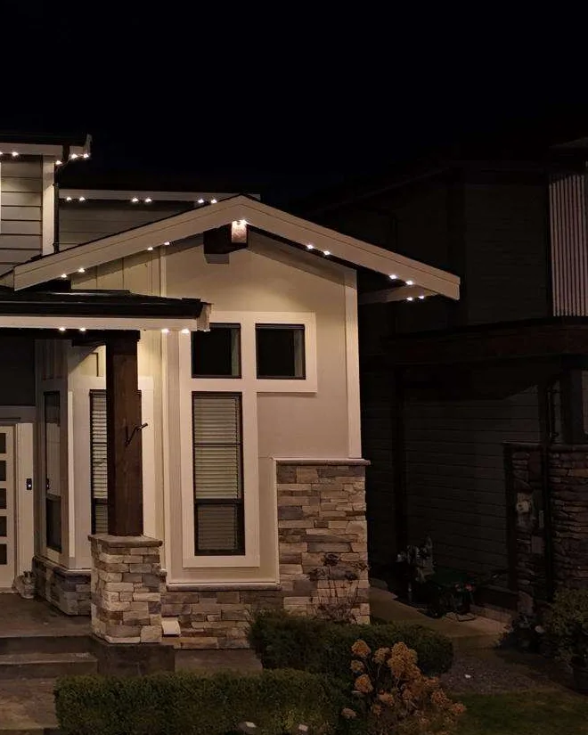 A gabled house at night with a warm white roofline and glowing front entrance.